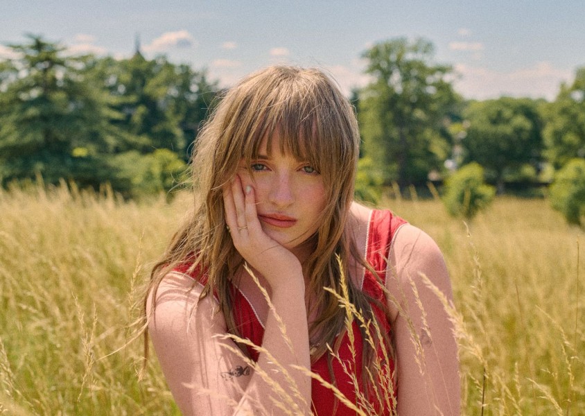 A woman in a red top with brown hair sat in a fieldx